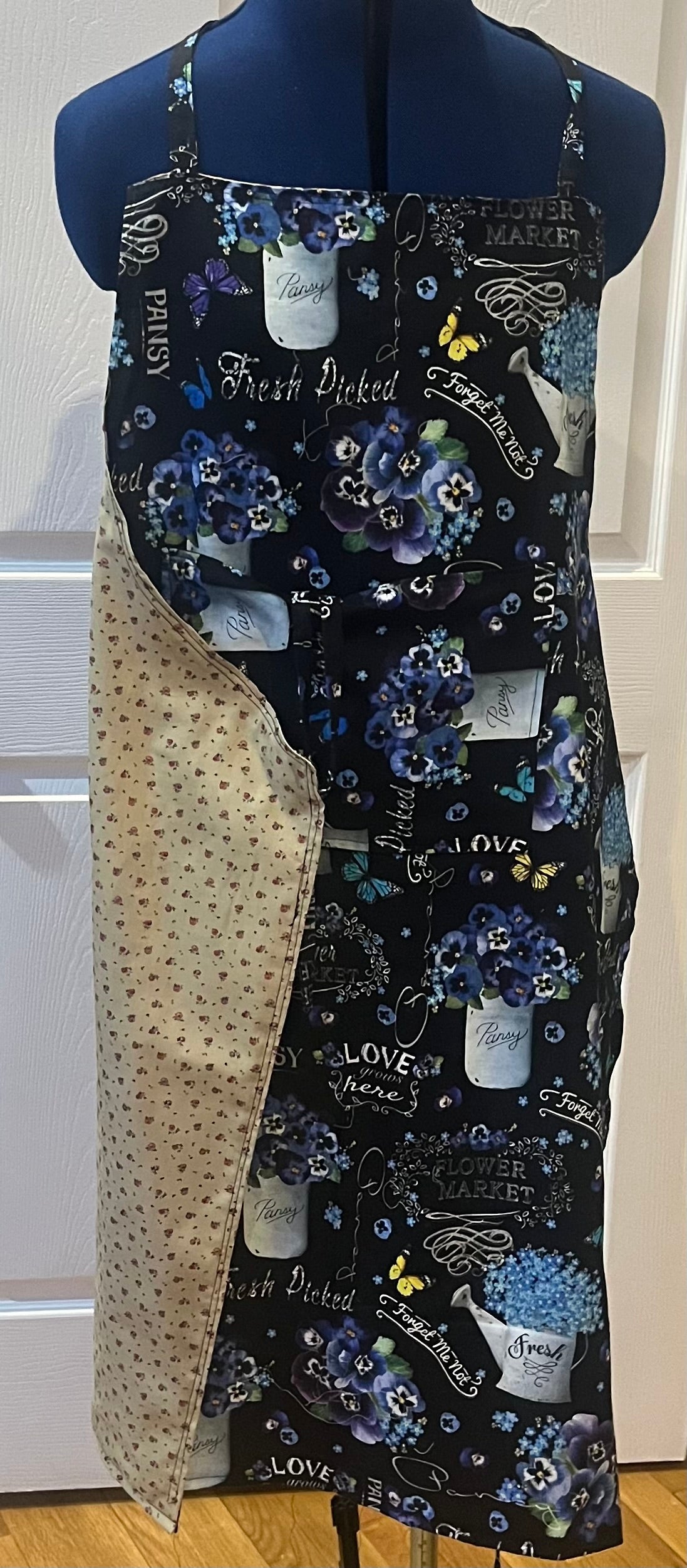 Flower market pansy bib apron showing black floral front and cream ditsy floral reverse
